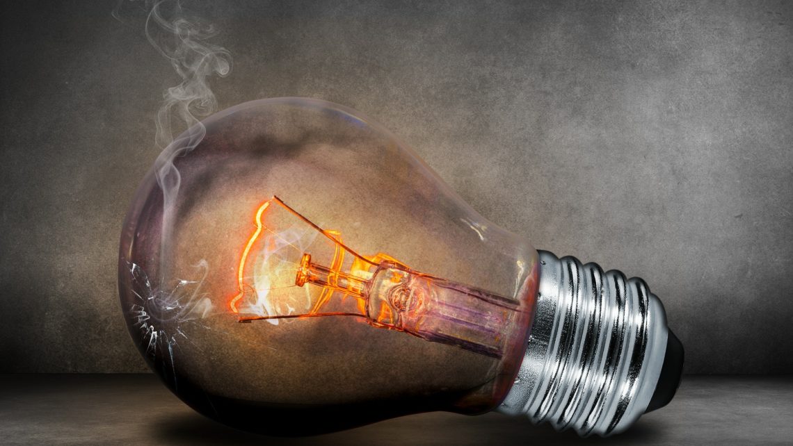 Incandescent light bulb on its side glowing reddish orange with a small broken hole in the glass and smoke coming out, representing failure and ideas