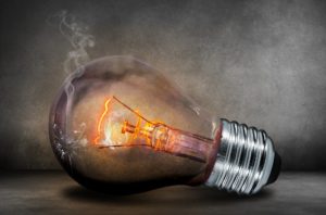 Incandescent light bulb on its side glowing reddish orange with a small broken hole in the glass and smoke coming out, representing failure and ideas