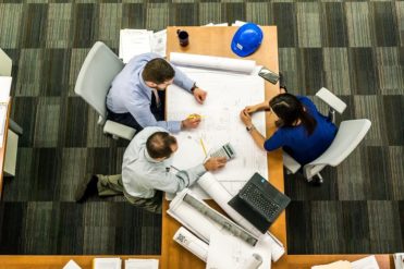 a group of people are sitting around a table looking at plan layout