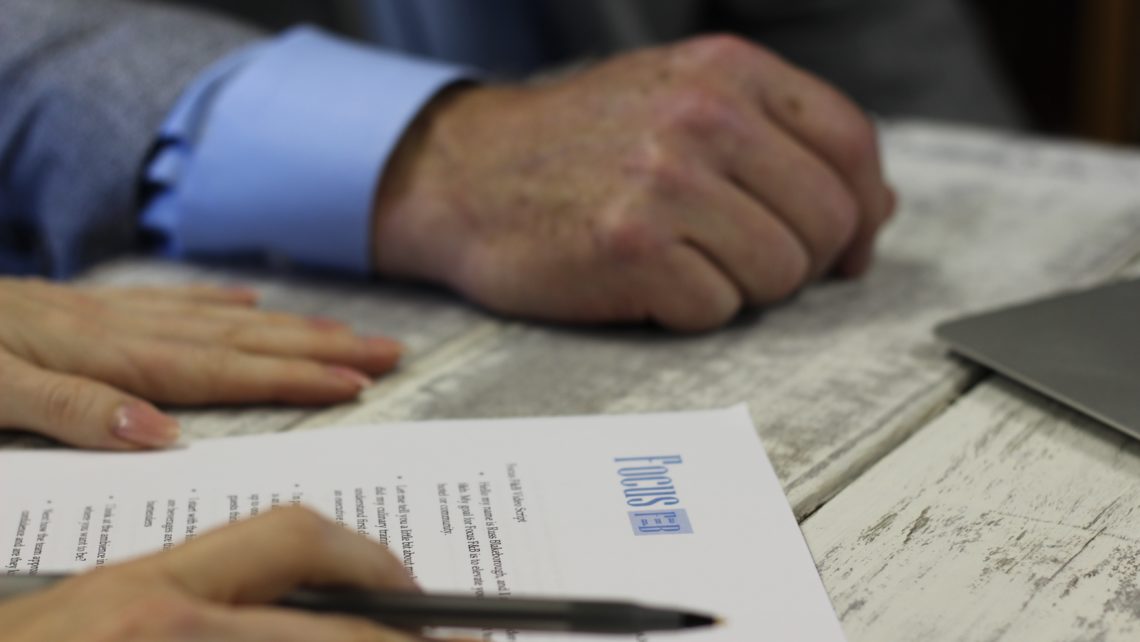 Two sets of hands on a table, one with a pen, looking at a report during a business meeting