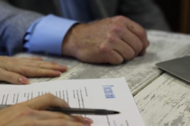 Two sets of hands on a table, one with a pen, looking at a report during a business meeting