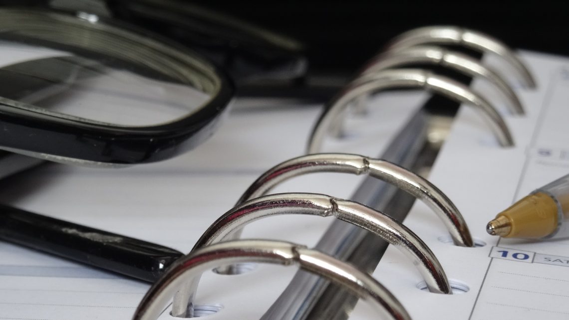 Close up view of a binder planner with glasses, a pen, ehs requirements