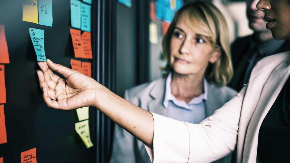 Meeting with people around a board of sticky notes working on software implementation