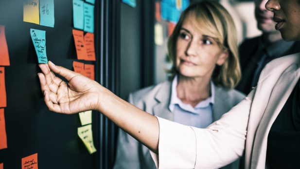 Meeting with people around a board of sticky notes working on software implementation